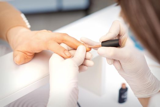 Hands of manicure master in white protective gloves apply polish to female fingernails