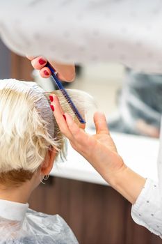 Female hairdresser styling short white hair of the young blonde woman with hands and comb in a hair salon