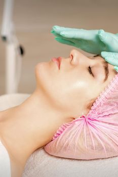 The woman is having cosmetic treatment during cosmetologist in medical gloves are touching the female face at the spa salon