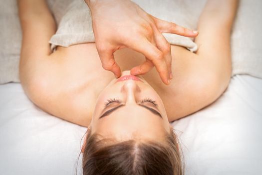 Young caucasian woman receiving chin massage by male therapist fingers in spa salon