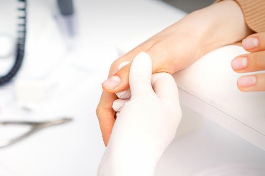 The manicurist holds the female thumb during a manicure procedure in the nail salon