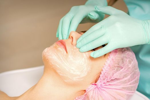A cosmetologist is applying cream on the female face, close-up view. Woman with doctor beautician in beauty clinic