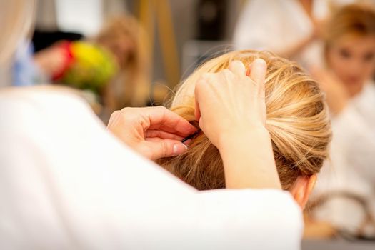 Hair stylist's hands doing professional hairstyling of female long hair in a beauty salon