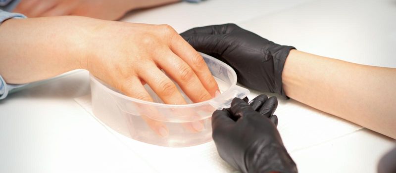 The female dipped her hand in a bowl of water softening nails preparing for the manicure