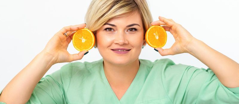 Portrait of young smiling blonde woman cosmetologist with halves of oranges on white background