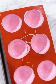 Filling in silicone chocolate molds with melted pink chocolate to prepare hot chocolate bombs.