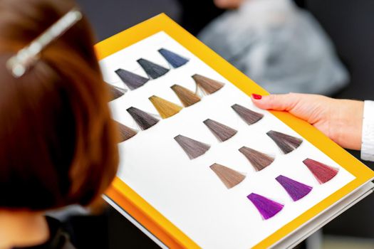 Young caucasian woman choosing a color from the hair color chart in a beauty salon
