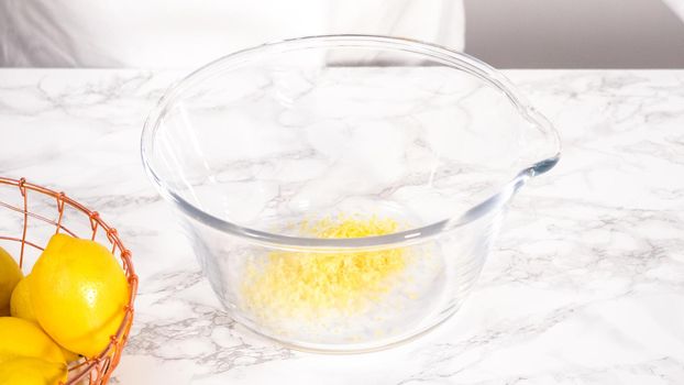 Step by step. Zesting fresh lemons into a glass mixing bowl to prepare lemon bundt cake.