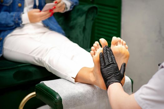 Moisturizing the feet. Hands of pedicure master in black gloves care about female feet. Foot massage. Pedicure beauty salon concept