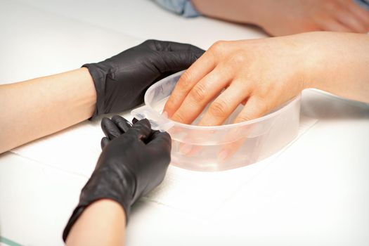 The female dipped her hand in a bowl of water softening nails preparing for the manicure
