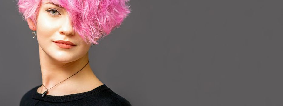 Portrait of beautiful young white woman with a pink short hairstyle on dark background with copy space