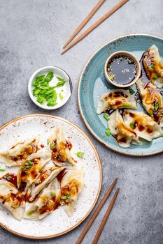 Close-up, top view of two plates with traditional Asian dumplings with soy sauce and chopsticks on gray rustic stone background. Authentic Chinese cuisine