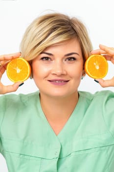 Portrait of young smiling blonde woman cosmetologist with halves of oranges on white background