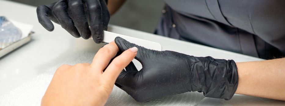 Woman receiving a manicure with nail file by a manicure master in a nail salon