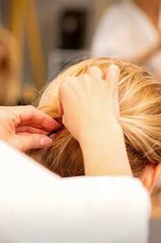 Hair stylist's hands doing professional hairstyling of female long hair in a beauty salon