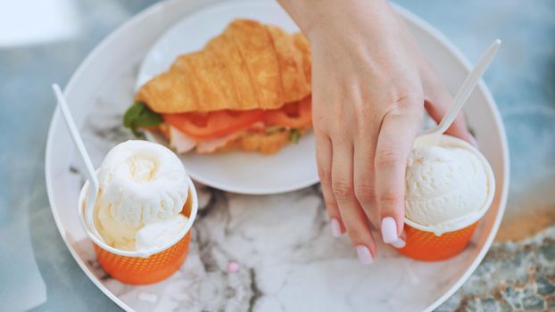 The girl takes the ice cream off the plate next to the croissant with the meat