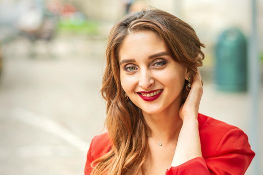 Portrait of a young white smiling woman standing in the red jacket and looking at the camera outdoors