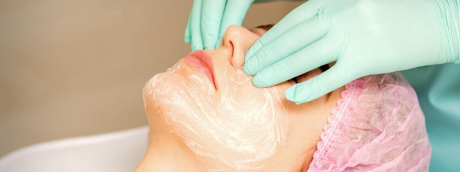 A cosmetologist is applying cream on the female face, close-up view. Woman with doctor beautician in beauty clinic