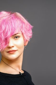 Portrait of beautiful young white woman with a pink short hairstyle on dark background with copy space