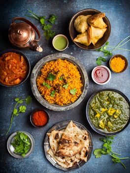 Top view of Indian traditional dishes and appetizers: chicken curry, pilaf, naan bread, samosas, paneer, chutney on rustic background. Table with choice of food of Indian cuisine, dinner/buffet