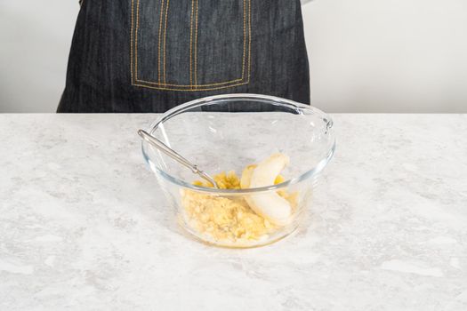 Smashing riped bananas in a glass mixing bowl to prepare coconut banana pancakes.