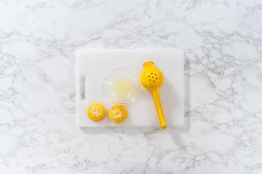 Zesting and juicing fresh lemon on a white cutting board.