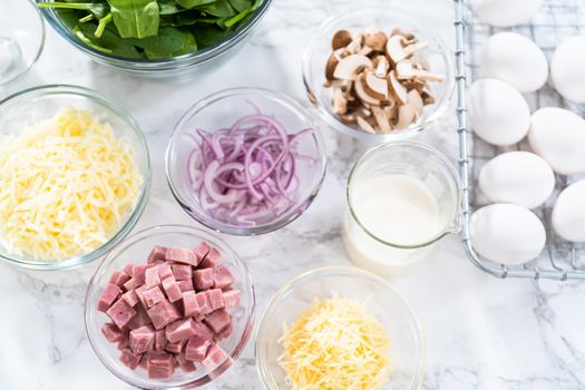 Ingredients in glass mixing bowls to prepare spinach and ham frittata.