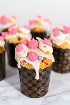 Freshly baked mini Easter bread kulich with lemon glaze, decorated with sprinkles and meringue bird-shaped cookies.