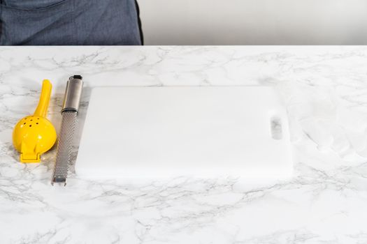 Zesting and juicing fresh lemon on a white cutting board.