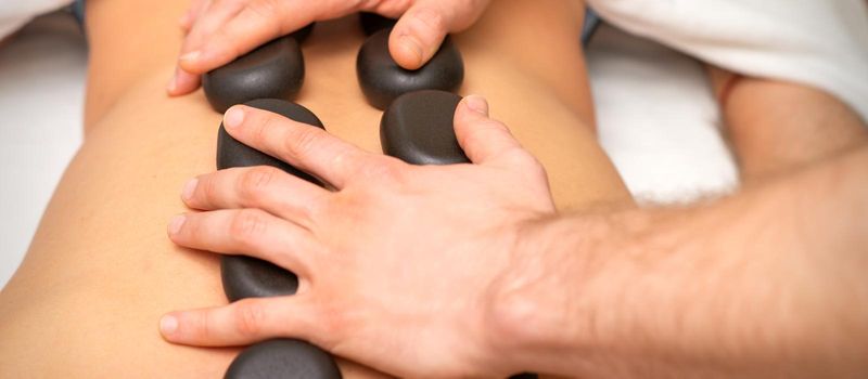 Young caucasian woman receiving back massage with black stones by masseur in spa salon. A woman getting a spa treatment