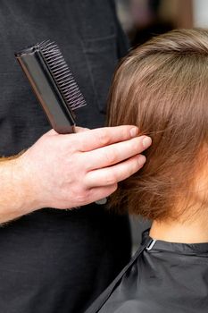 Male hairdresser works on the hairstyle of the young caucasian brunette woman at a hair salon