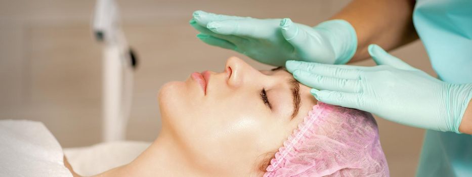 The woman is having cosmetic treatment during cosmetologist in medical gloves are touching the female face at the spa salon