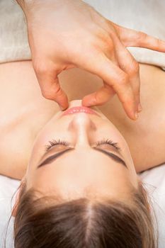 Young caucasian woman receiving chin massage by male therapist fingers in spa salon