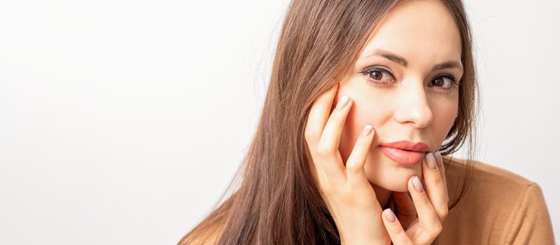 Portrait of the caucasian female model touching face with manicured fingers isolated on white background