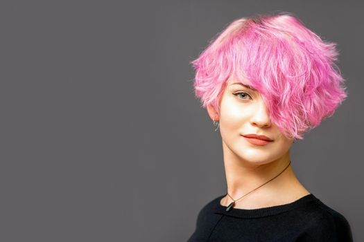 Portrait of beautiful young white woman with a pink short hairstyle on dark background with copy space