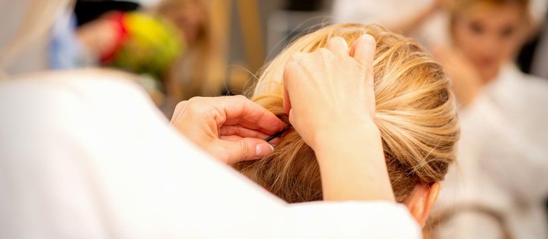 Hair stylist's hands doing professional hairstyling of female long hair in a beauty salon