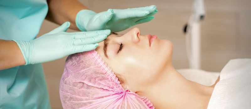 The woman is having cosmetic treatment during cosmetologist in medical gloves are touching the female face at the spa salon