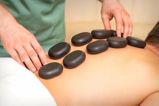 Young caucasian man receiving back massage with black stones by masseur in spa salon. A man getting a spa treatment