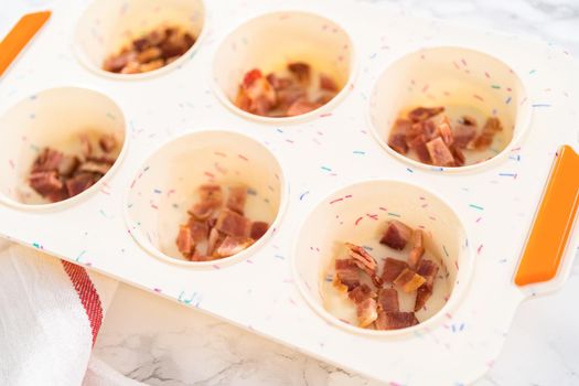 Filling silicone muffin pan with ingredients to bake bacon and cheese egg muffin.