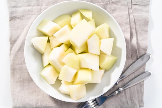 Sliced golden dewlicious melon in a white bowl.