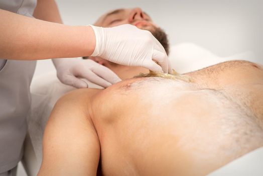 Epilation chest of a young male with the liquid wax paste in a beauty salon