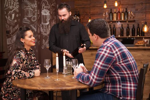 Hipster bearded bartender showing a bottle of wine to clients in vintage hipster pub or restaurant