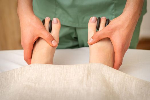 Massager doing feet and toes massage with rocks between a female toes