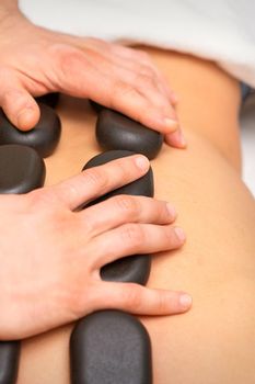 Young caucasian woman receiving back massage with black stones by masseur in spa salon. A woman getting a spa treatment