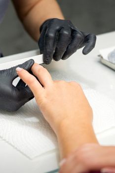 Woman receiving a manicure with nail file by a manicure master in a nail salon