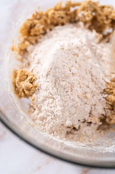 Mixing ingredients in a large glass mixing bowl to bake apple oatmeal cookies.