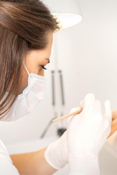 Manicure master in protective face mask and white gloves apply polish to female fingernails