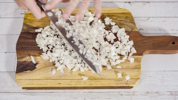 Mincing organic yellow onion on a wood cutting board.