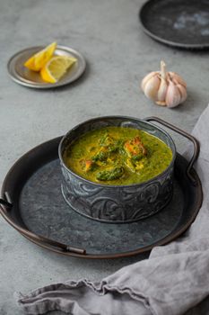 Traditional vegetarian Indian Punjabi food Palak Paneer with spinach and cheese in vintage metal bowl with spoon on rustic grey concrete background table, angle view
