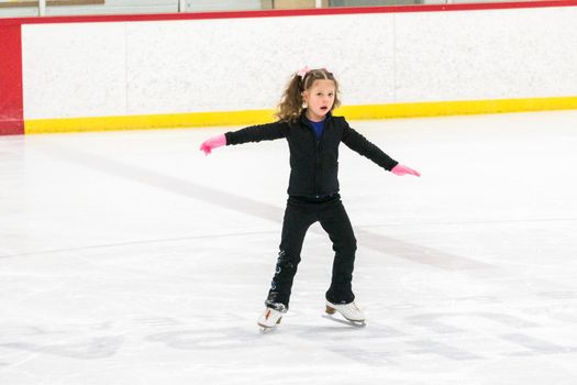 Little girl practicing figure skating moves on the indoor ice rink.